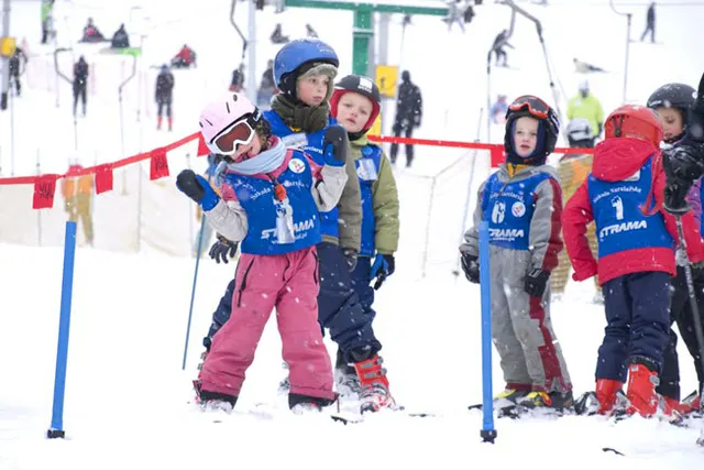 Children in helmets and ski school bibs waiting their turn on the nursery slope