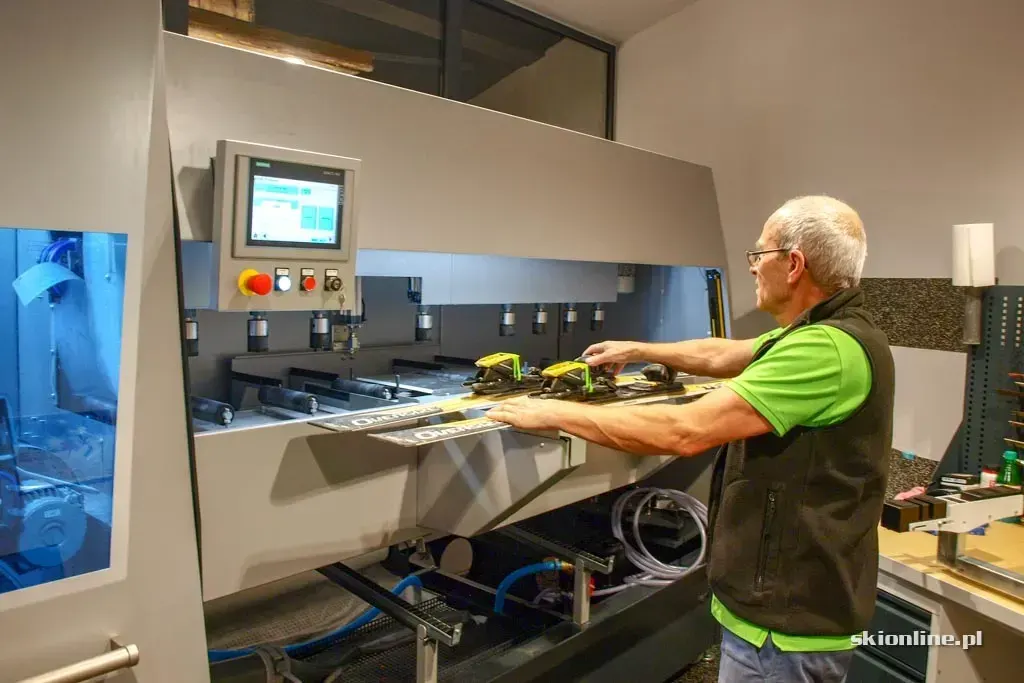 A technician feeds a ski into a service machine at a rental shop by the slopes