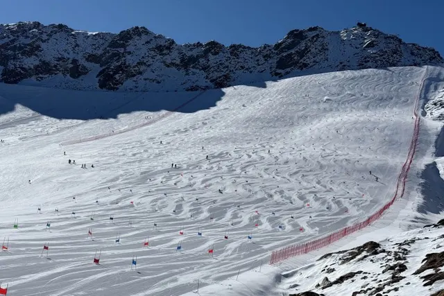A wide piste on the Val Senales glacier at Maso Corto, with skiers at varying distances and slalom poles along the safety net
